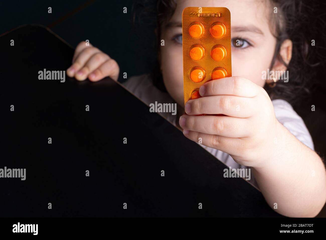 Ein kleines Mädchen, das ein Multivitamin-Loaf von Tabletten vom Tisch pflückt und die Gefahr von Pillen durch Kinder von einem Konzept isst Stockfoto