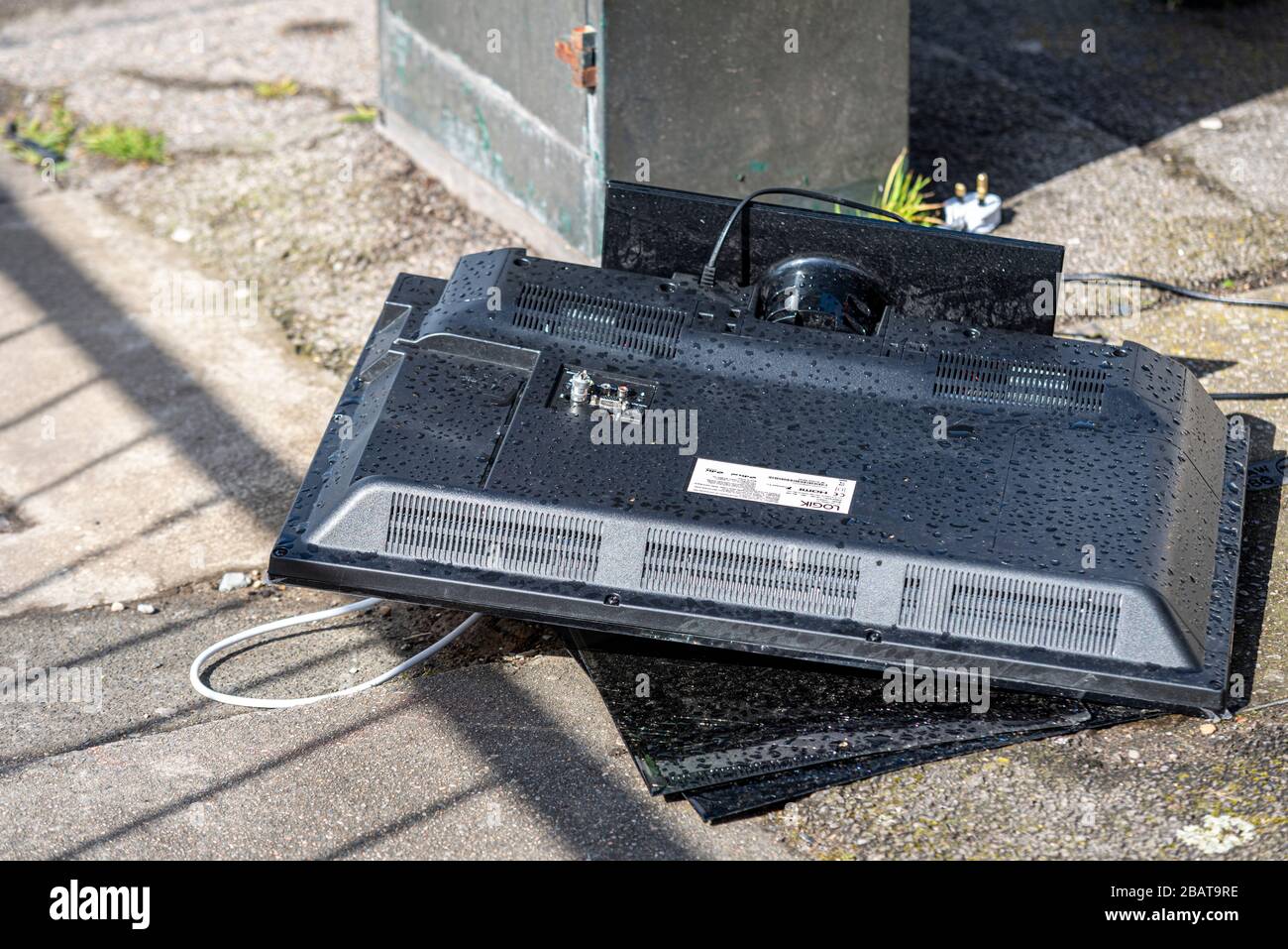 Ausrangierter Flachbildfernseher zerschlug sich auf einem Straßenpflaster. Elektroschrott wird im Regen ins Freie entsorgt. Logik TV mit angeschlossenem Stecker Stockfoto