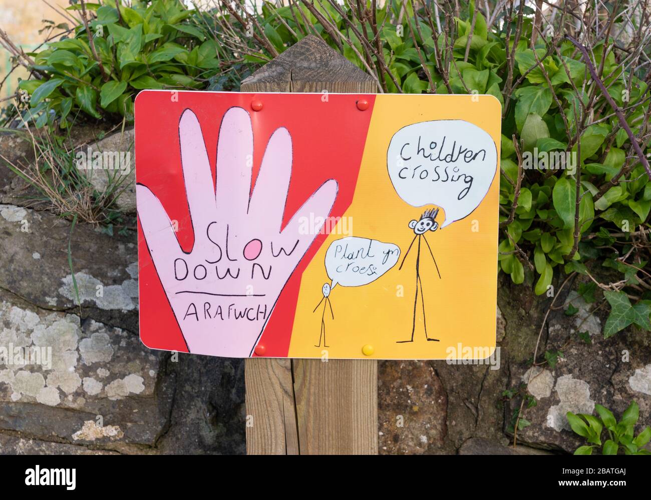 Ein handgezeichnetes Schild außerhalb einer Schule, das auf Englisch und Walisisch rät, sich mit dem Überqueren von Kindern zu verlangsamen. Newport, Pembrokeshire. Wales. GROSSBRITANNIEN Stockfoto