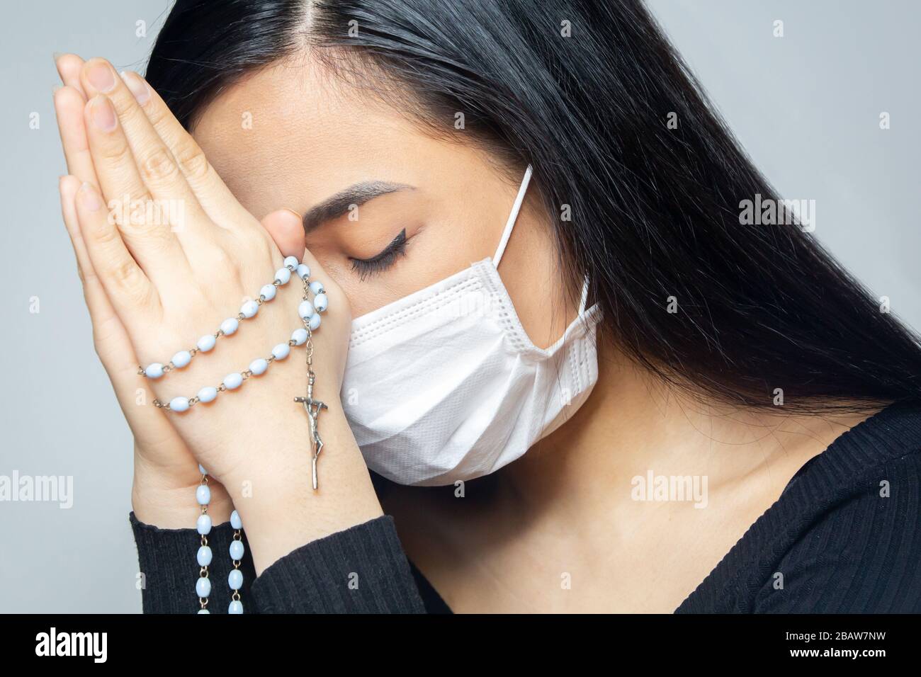 Eine Frau mit medizinischer Maske, die über die globale Coronavirus-Pandemie betet, um Angst und Depression zu reduzieren. Frau mit Rosenkranz. Stockfoto
