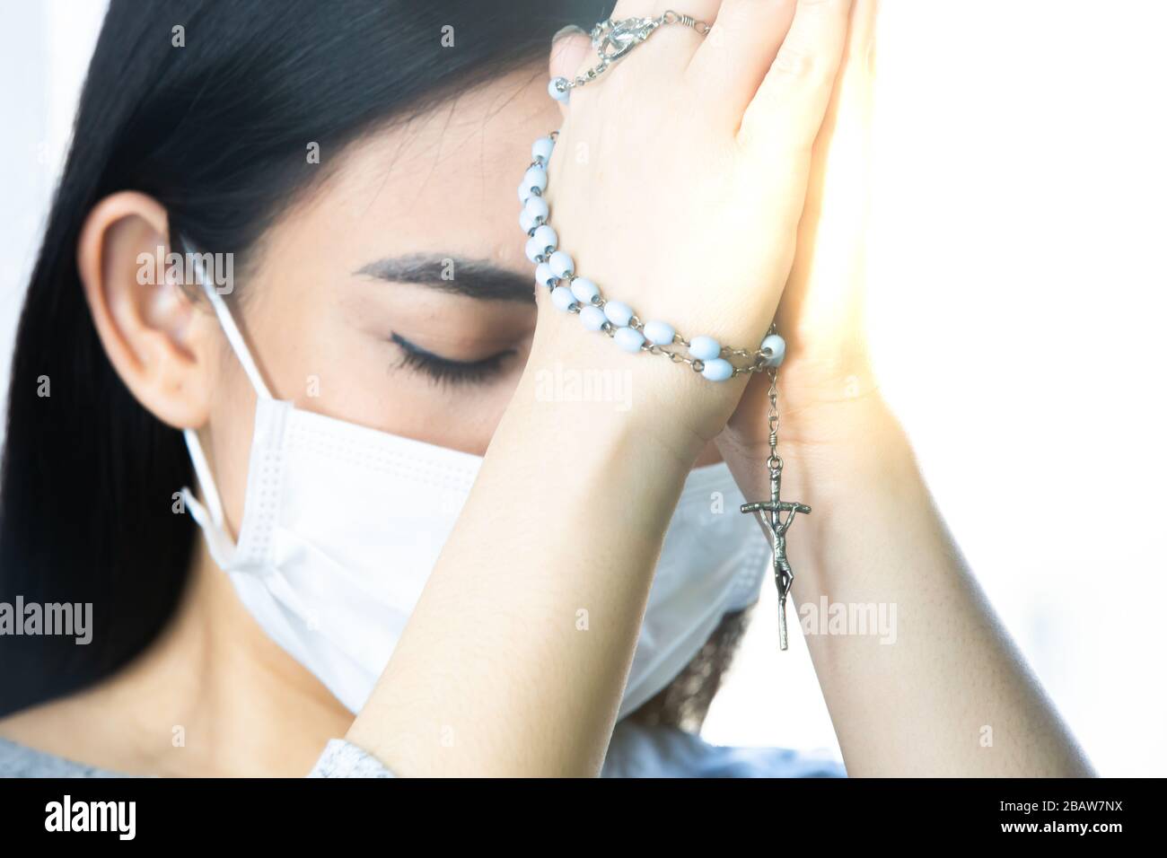 Eine Frau mit medizinischer Maske, die über die globale Coronavirus-Pandemie betet, um Angst und Depression zu reduzieren. Frau mit Rosenkranz. Stockfoto