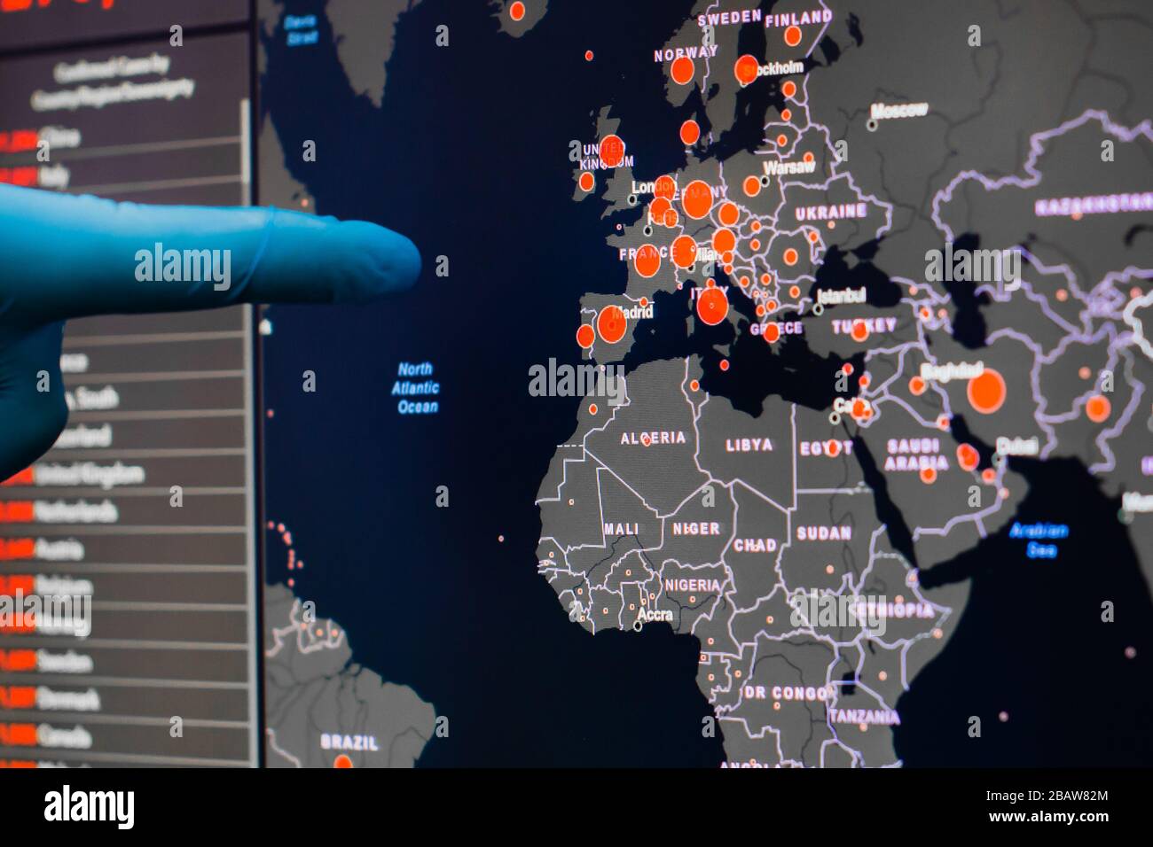 Ein Mann mit blauen Handschuhen zeigt auf einem Bildschirm mit Europakarte von Coronavirus, SARS-COV-2. Bestätigte Fälle von Coronavirus-Krankheit in der Welt. Bericht Stockfoto
