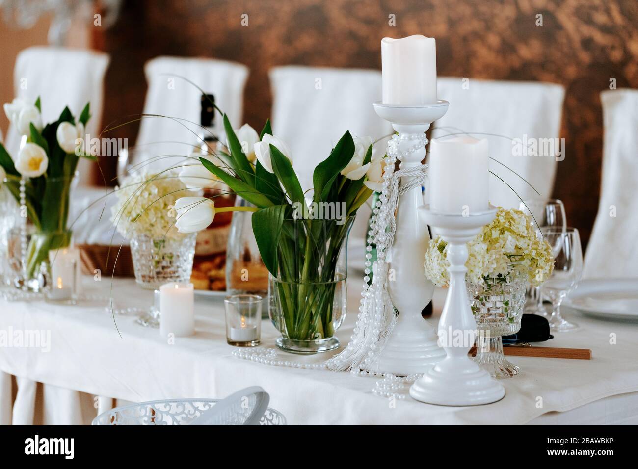 Dekoration einer Hochzeit, weiße Blumen, Kerzen und Brille für Getränke Stockfoto
