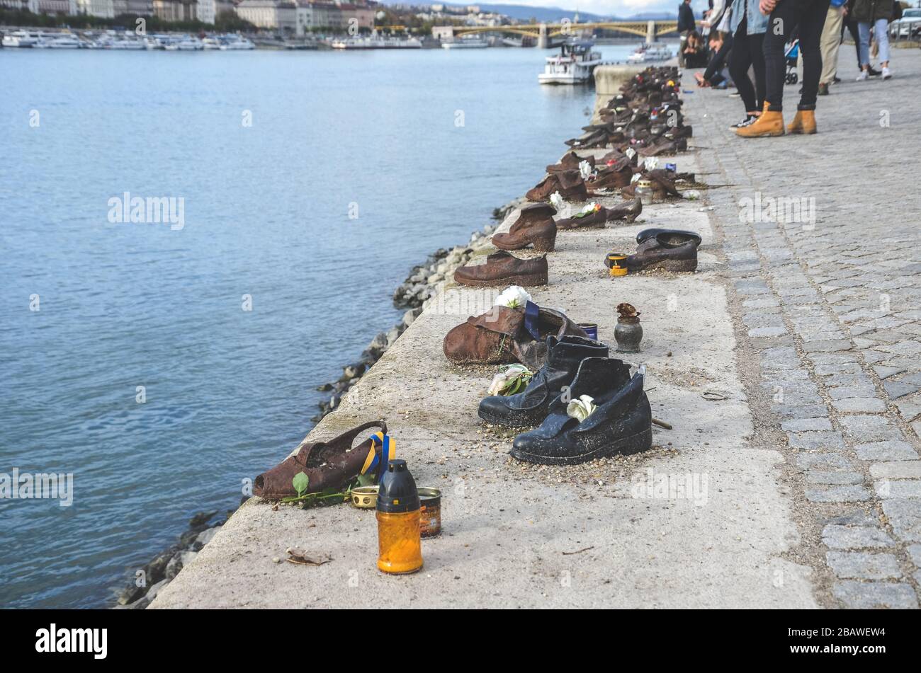 Budapest, Ungarn - 6. November 2019: Schuhe an der Donau-Bank. Denkmal zur Ehrung der Juden, die im zweiten Weltkrieg von Faschisten getötet wurden Eisenschuhe. Verschwommene Donau und Touristen im Hintergrund. Stockfoto