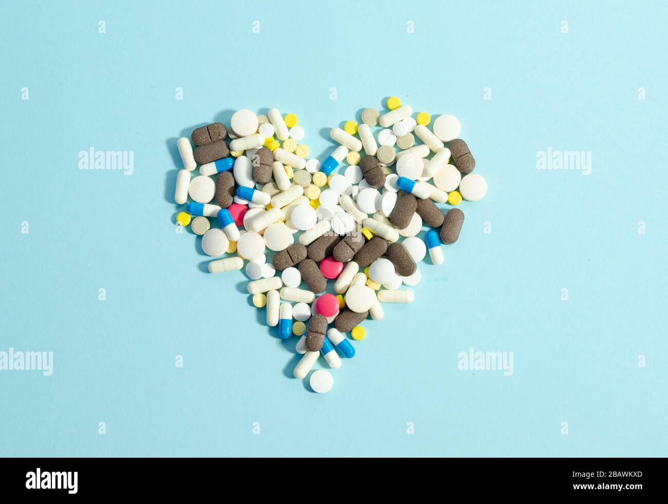 Pillen, die in Herzform auf blauem Hintergrund liegen. Verschiedene Pillen zusammen. Stockfoto