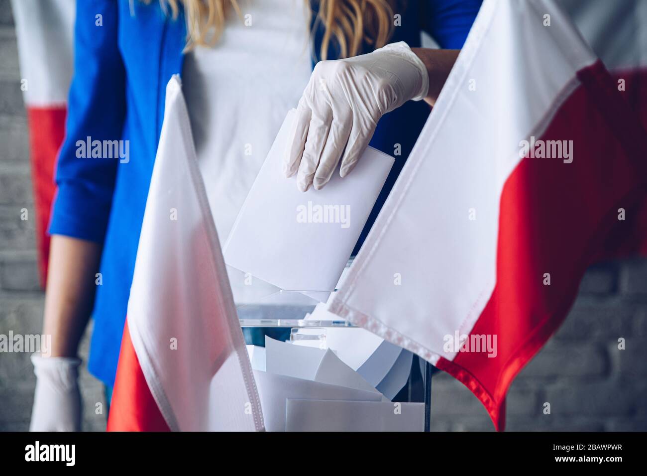 Frau in Schutzhandschuh, die ihre Stimme auf die Wahlurne setzt Stockfoto