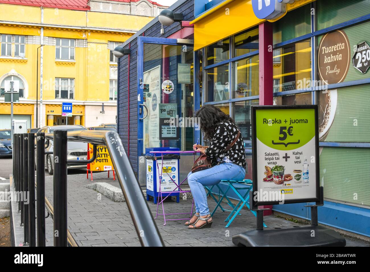 Eine Frau sitzt und schreibt an einem kleinen Terrassentisch im Freien vor einem Laden in Porvoo, Finnland. Stockfoto