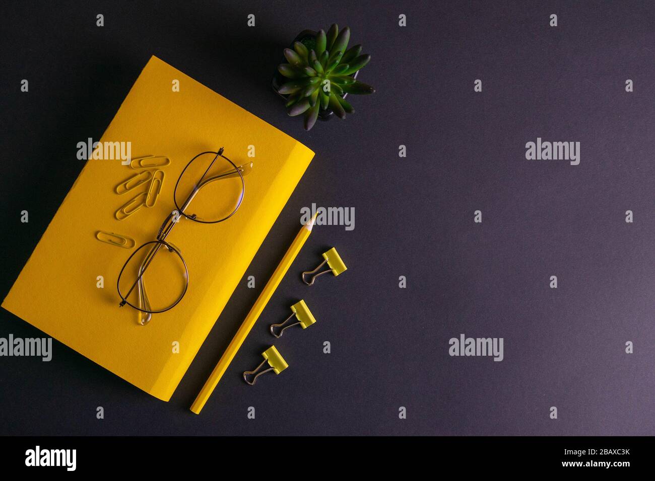 Gelber Bleistift, gelbes Notizbuch und Brille, Stifte, Clip-Papier auf schwarzem Hintergrund Stockfoto