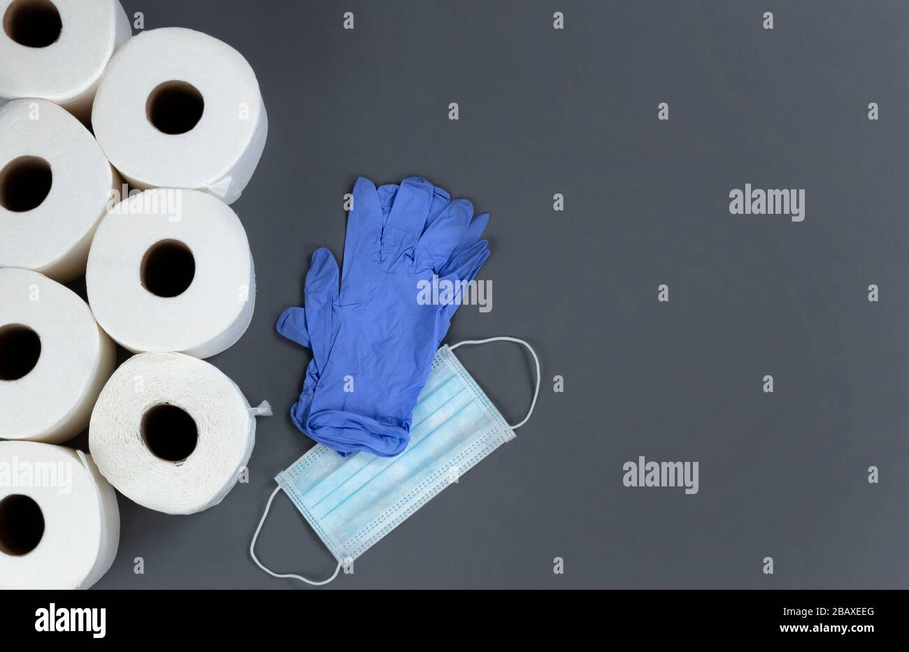 Vorräte wie toilettenpapier, Maske und Handschuhe zum Überleben gegen COVID-19 oder Coronavirus auf grauem Hintergrund. Stockfoto