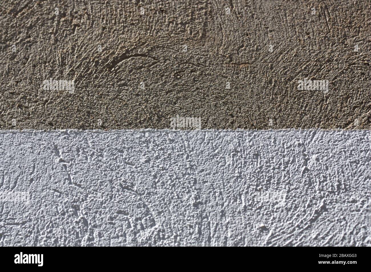 Bild einer Betonwand, die einen Teil davon weiß lackiert hat und das Bild in zwei verschiedene farbige Texturen teilt Stockfoto