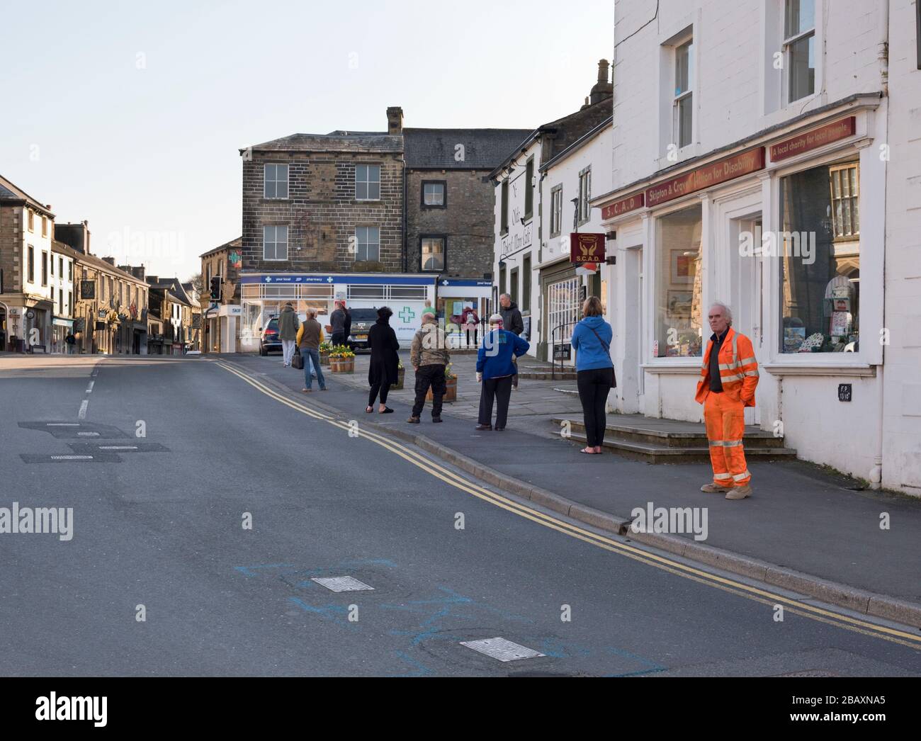 Coronavirus Shutdown, Settle, North Yorkshire. Eine Warteschlange für den örtlichen Chemieladen mit sozialer Distanzierung erstreckt sich über die Hauptstraße. Stockfoto