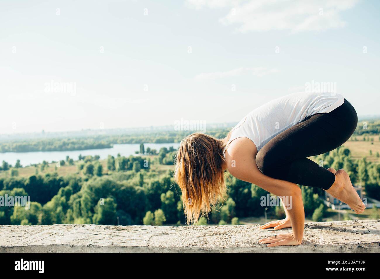 Junge Frau übt draußen Yoga. Blonde Mädchen posieren auf Brüstung auf  schöner Aussicht Bakasana oder Kran. Sie kleidete sich in schwarze  Beinkleider und weißes T Stockfotografie - Alamy