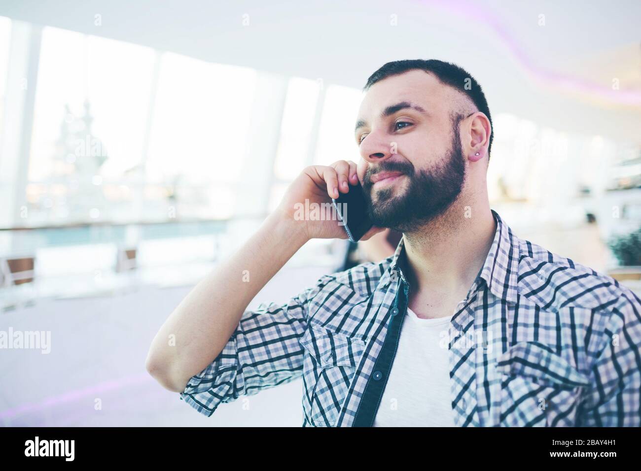 Seitenansicht des jungen bärtigen Mannes, in grauer Strickjacke gekleidet, sitzt am runden Holztisch im Café mit modernem Interieur und hält Smartphone Stockfoto