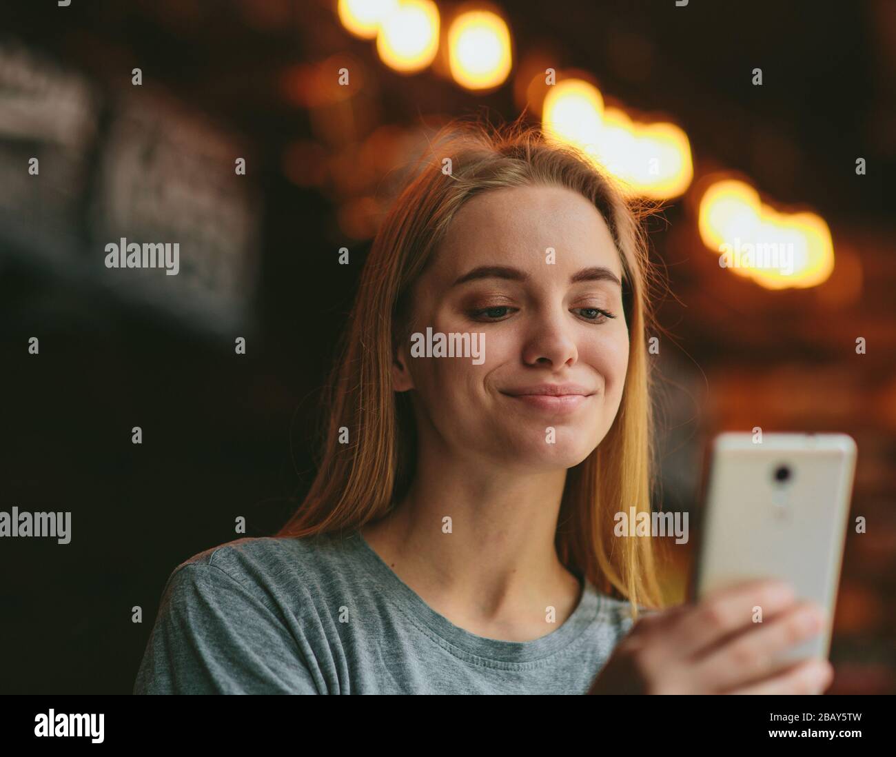 Schöne junge Frau im Café oder Restaurant halten Smartphone in der Hand und sehen es mit einem Lächeln an. Fröhliche fröhliche weibliche Person mit modernen Technologien. Stockfoto