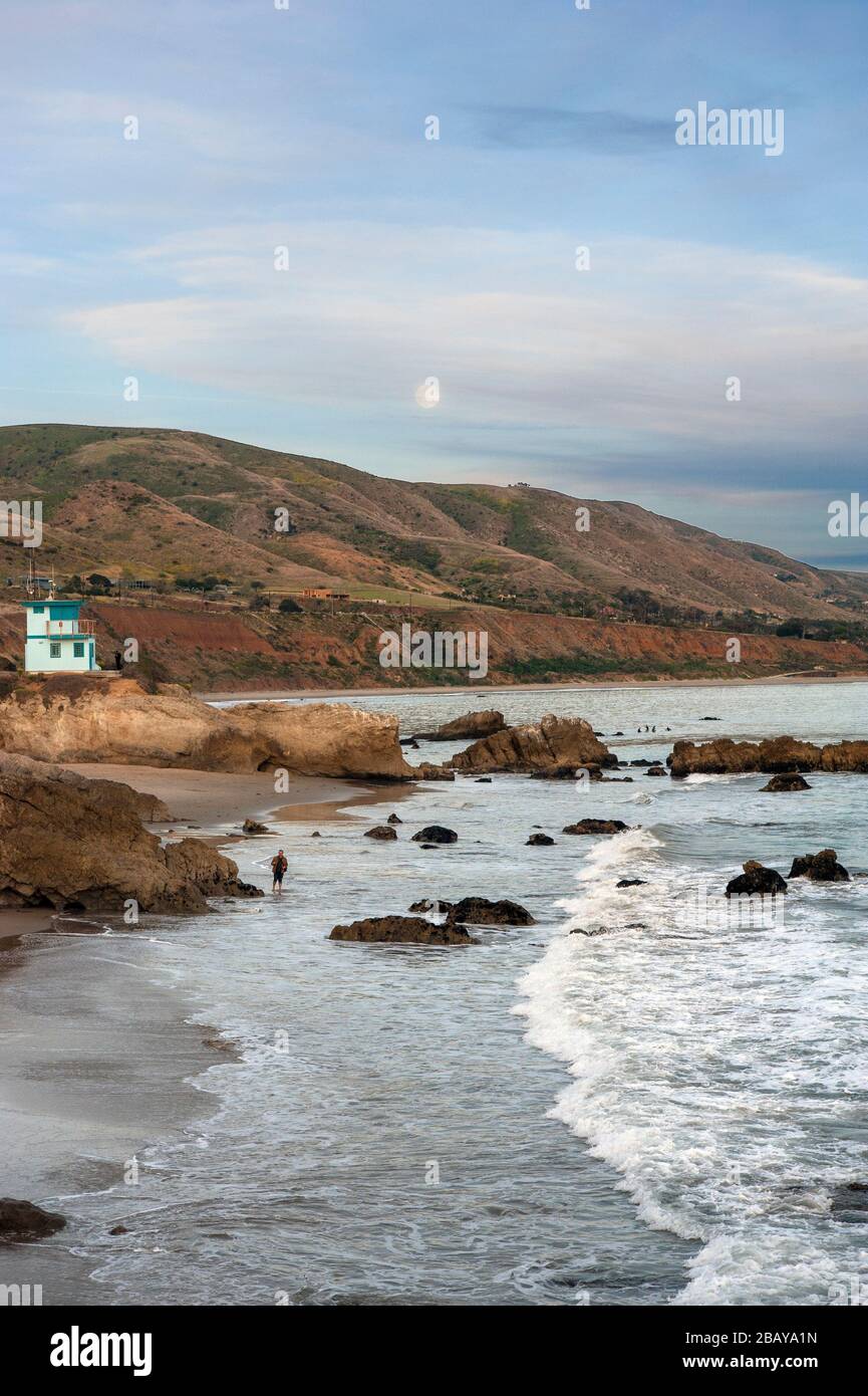 Mann, der an einem Strand in Malibu spazieren geht und den Vollmond über die Küstenhügel entlang der Küste Südkaliforniens, USA, erhebt Stockfoto