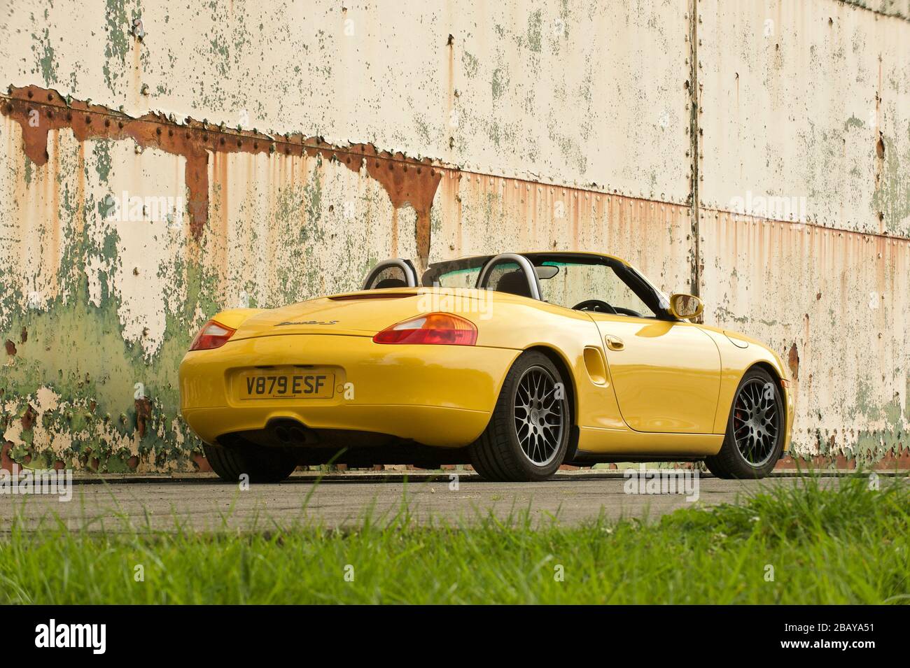 Gelber Porsche Boxster gegen texturierte Hangartüren, hinterer Dreiviertelwinkel Stockfoto