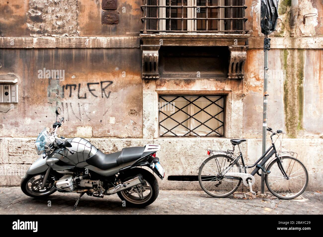 Ein Motorrad, Fahrrad und ein anti-semitisches Graffiti auf einer Seitenstraße in Rom, Latium, Italien, Europa, Farbe Stockfoto