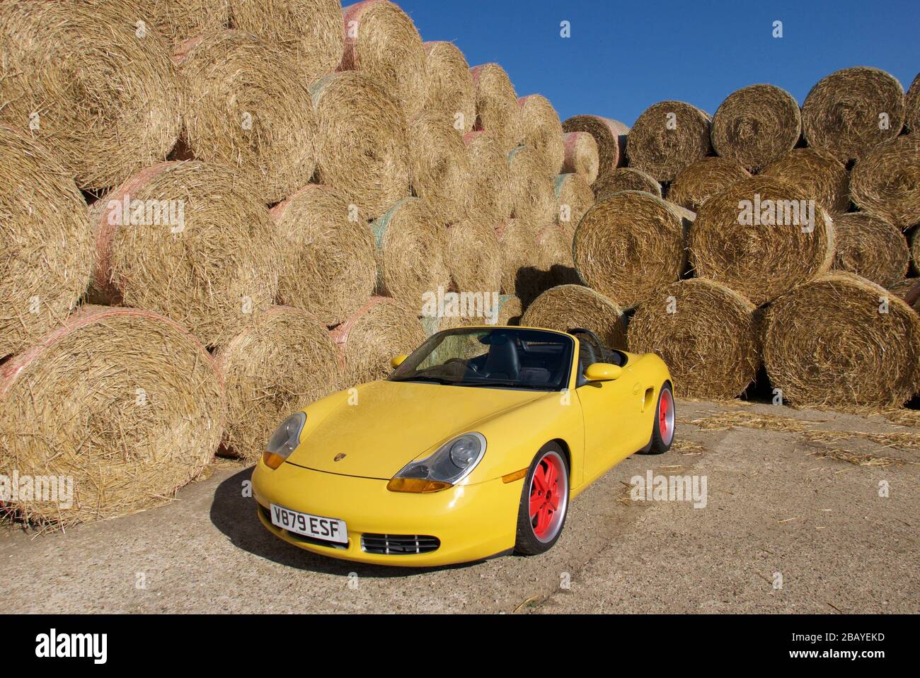 Gelber Porsche Boxster, dreiviertel vorn, gegen die Wand aus runden Strohballen Stockfoto