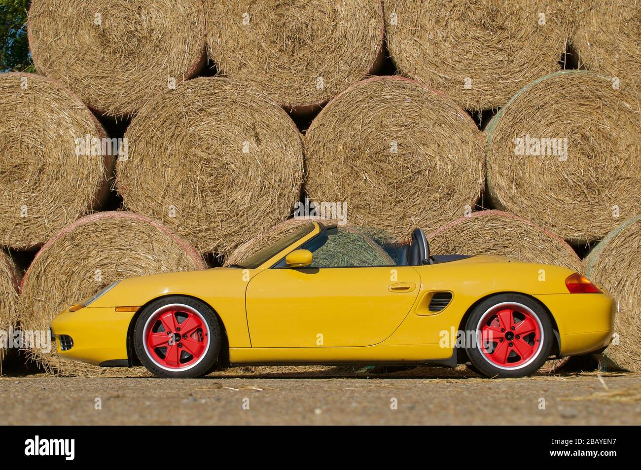 Gelber Porsche Boxster, dreiviertel vorn, gegen die Wand aus runden Strohballen Stockfoto