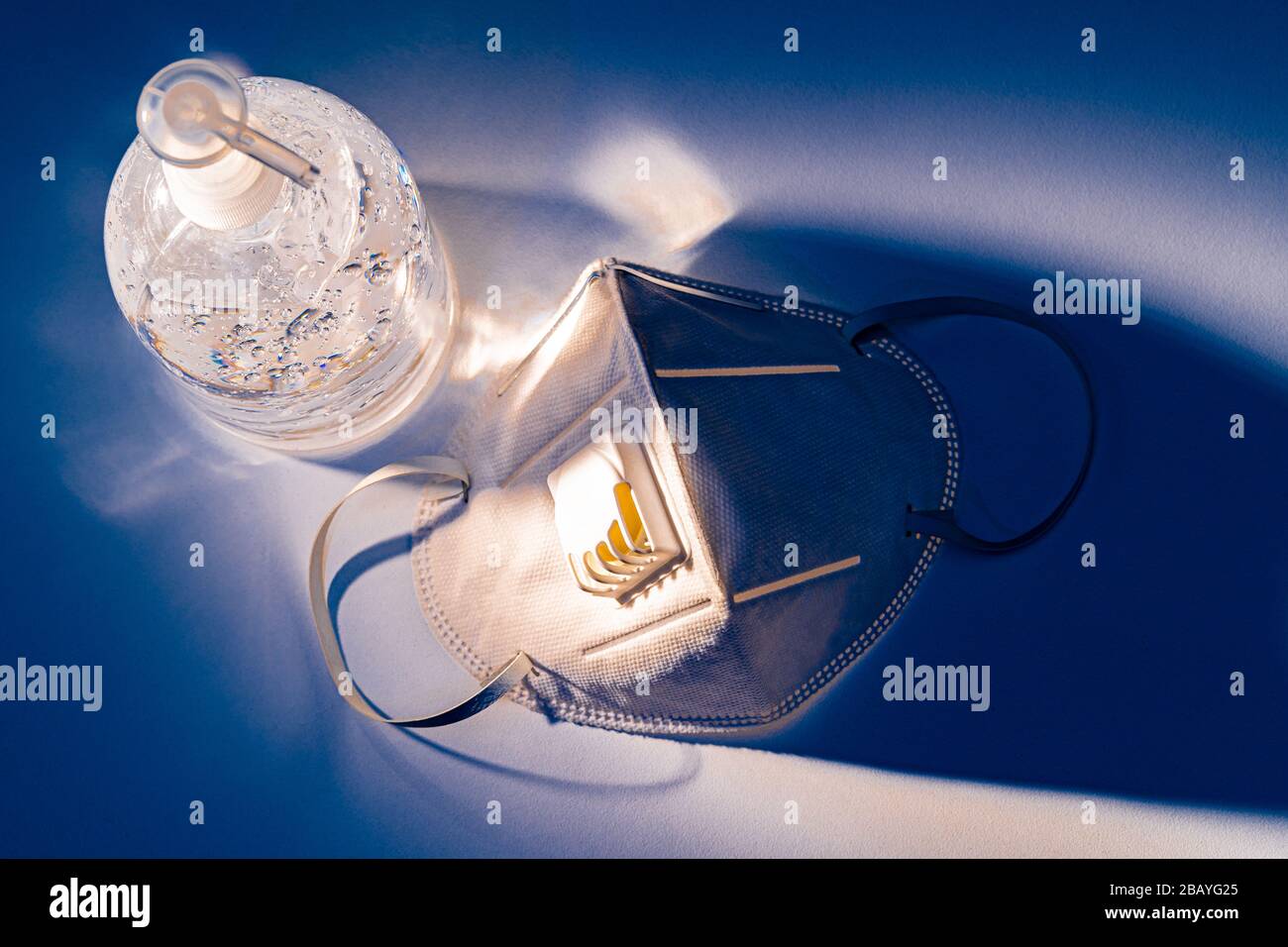 Antiseptisches Handgel und N95-Maske auf weißem Tisch mit dramatischem blauen Lichteffekt, Gesundheitskonzept Stockfoto
