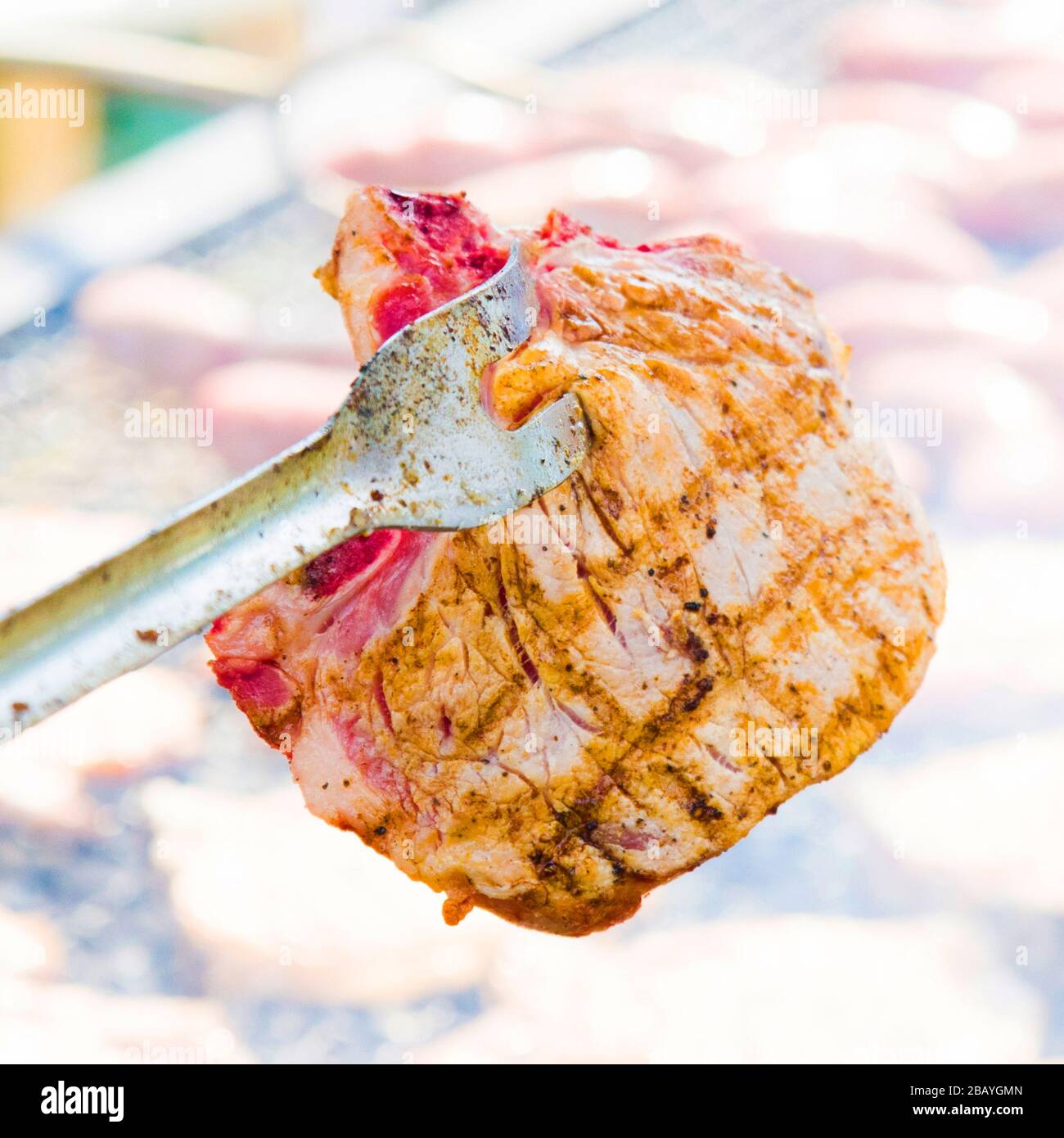 Würstchen und Schweinesteaks auf einem großen Barbaque mit heißen Kohlen und aromatischen Kräutern gekocht Stockfoto