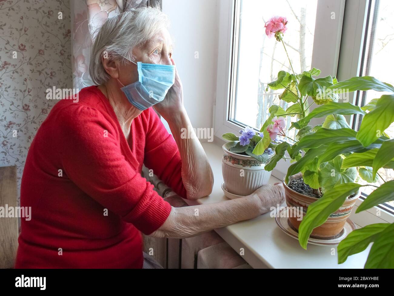 Das Konzept von Covid-19, Gesundheit, Sicherheit und Pandemie - ältere, einsame Frau, die in der Nähe des Fensters sitzt Stockfoto