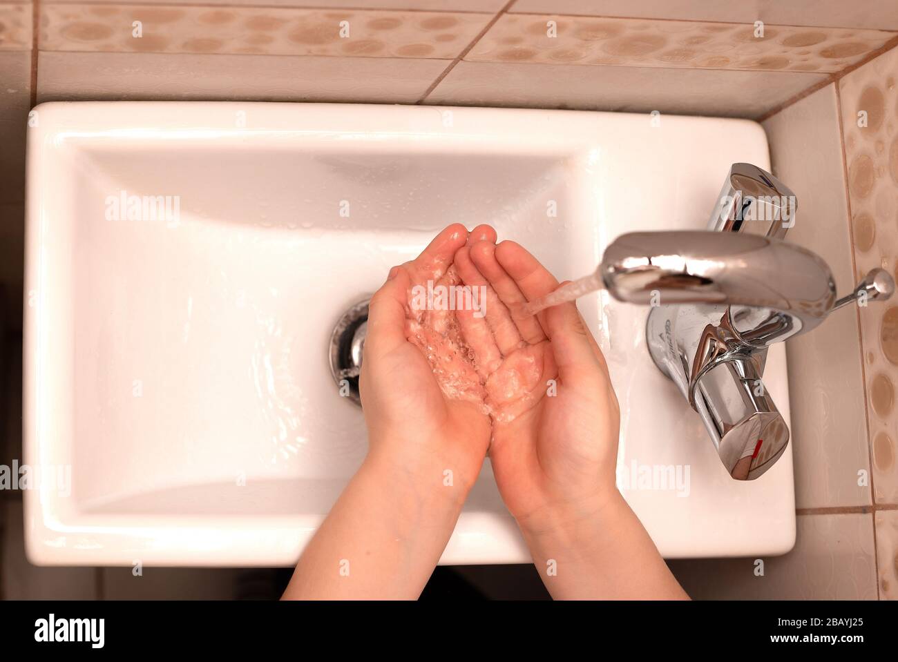Die Hände der Kinder über dem Waschbecken im Badezimmer mit strömendem Wasser. Draufsicht. Nahaufnahme Stockfoto