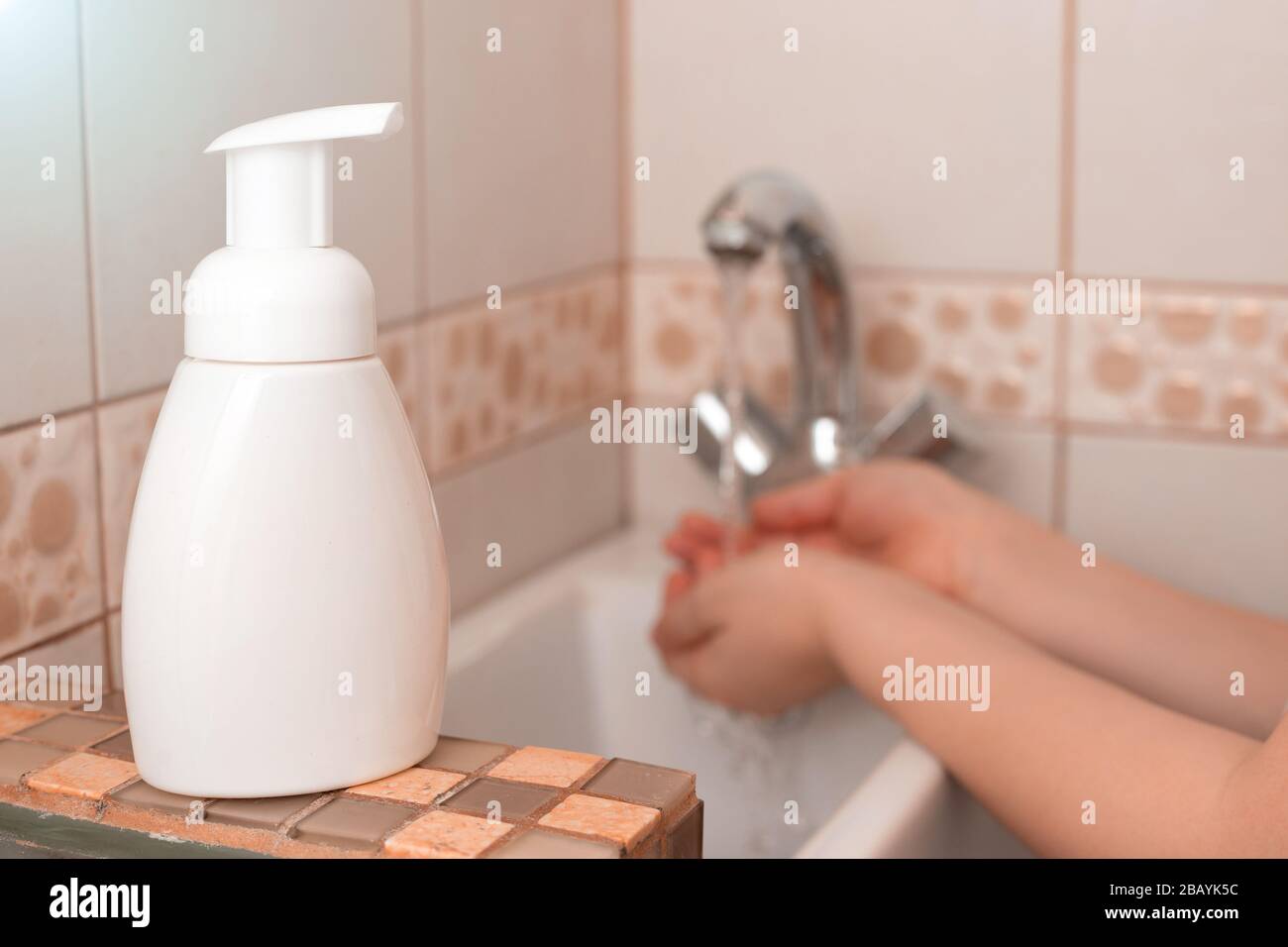 Eine weiße Flasche mit antibakterieller Seife steht in der Nähe der Spüle, die Kinder über ein Waschbecken in einer Badewanne mit Wasser in loser Schüttung führen. Nahaufnahme. Verspotten Sie sich. Selektiv Stockfoto