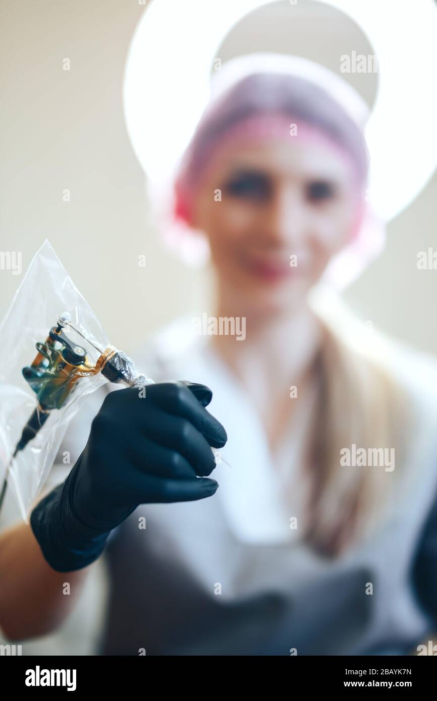 Frau Schönheitsmeister hält Nadel für permanente Make-up-Tattoo-Pistolen-Hände in schwarzen Handschuhen. Einsatzbereit Stockfoto