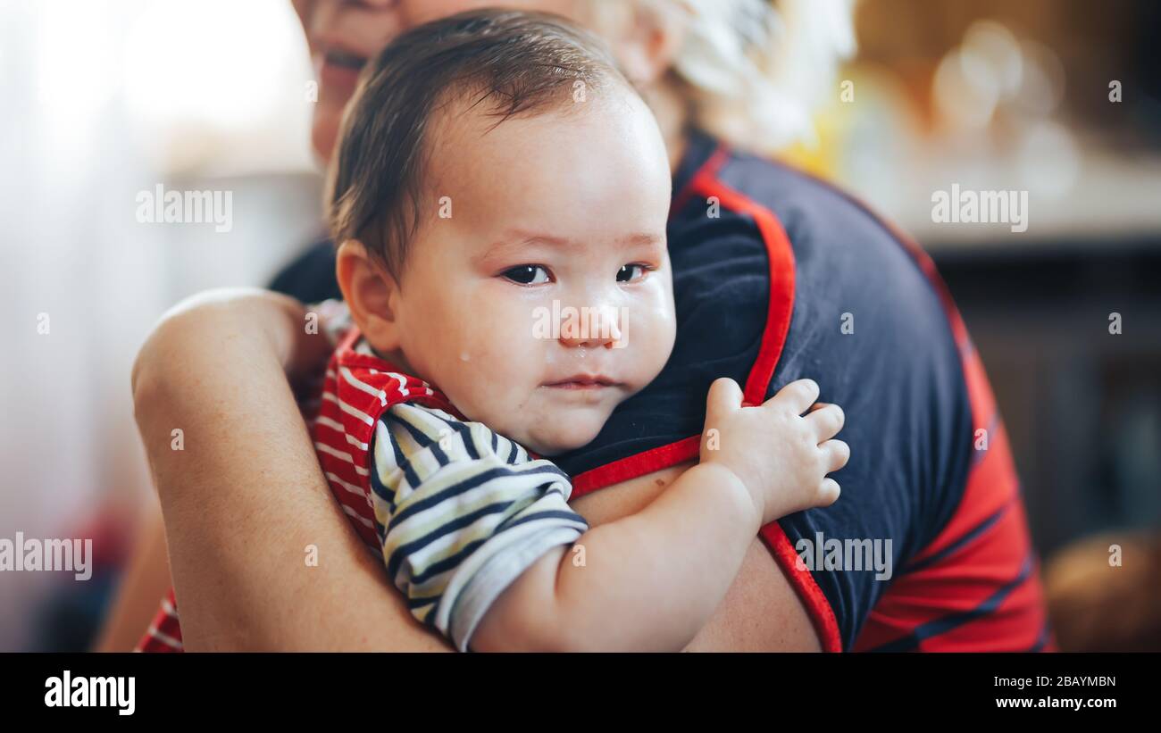 Großmutter, die weinendes Mädchen im Säuglingsalter mit Blick auf die Kamera umschlindet Stockfoto