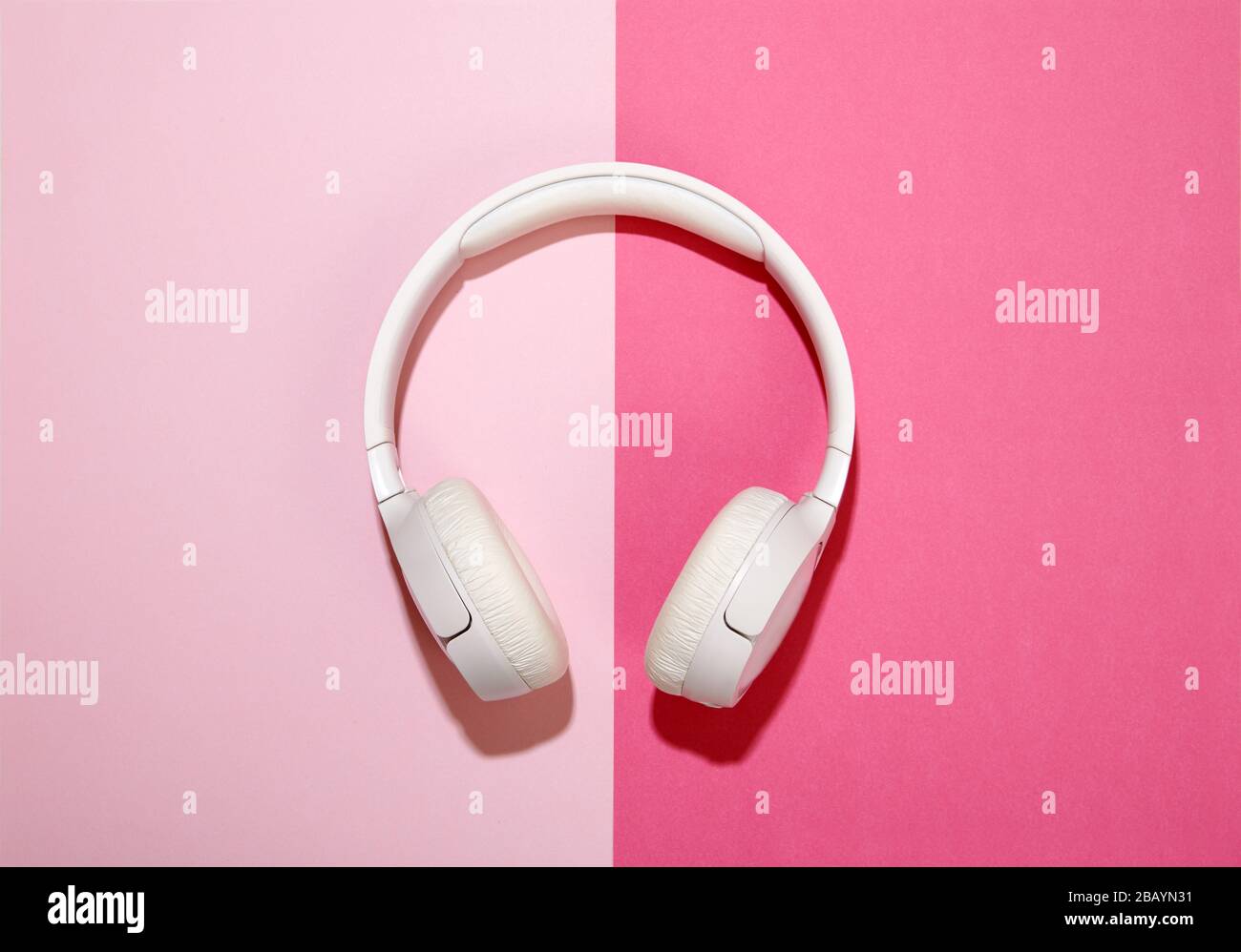 Weiße Kopfhörer auf einem duofarbenen, rosafarbenen Hintergrund, der über der Mitte mit seitlichem Kopierraum platziert ist Stockfoto
