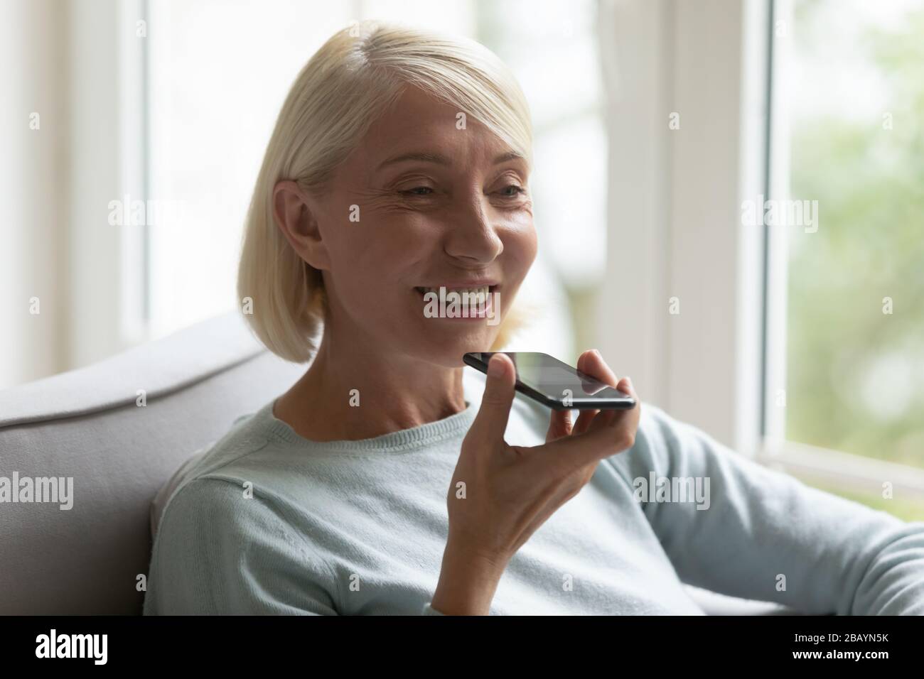 Lächelnde Frauen mittleren Alters verwenden Sprachassistenten auf dem Smartphone Stockfoto