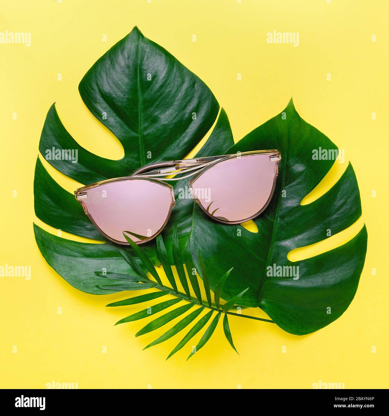 Sommerliche Zusammensetzung tropischer Palmenblätter, Monstera. Gelber Hintergrund mit rosafarbener Brille. Konzept - Sommerurlaub Stockfoto