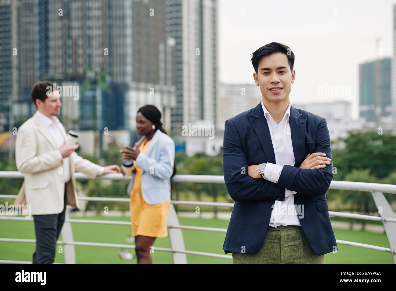 Portrait junger, gutaussehender vietnamesischer Geschäftsmann, der sich über die Arme querte und beim stehen im Freien die Kamera ansah Stockfoto