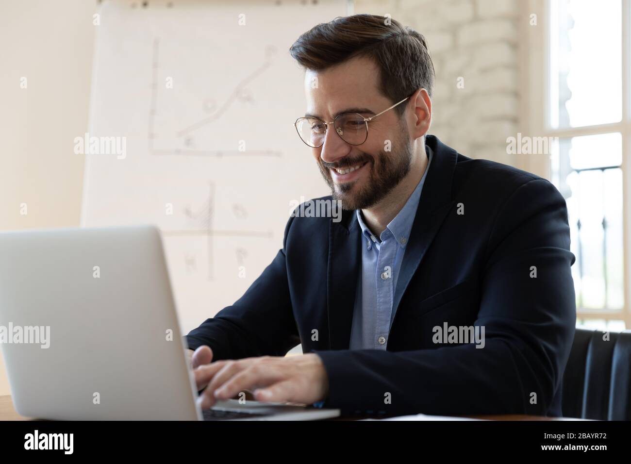 Lächelnder Geschäftsmann, der auf einem Laptop tippt und am Arbeitsplatz sitzt Stockfoto