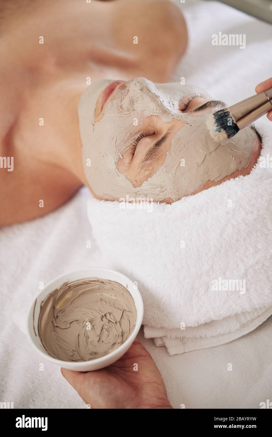 Kosmetologe wendet Schlammmaske auf Gesicht des jungen Mannes an Stockfoto