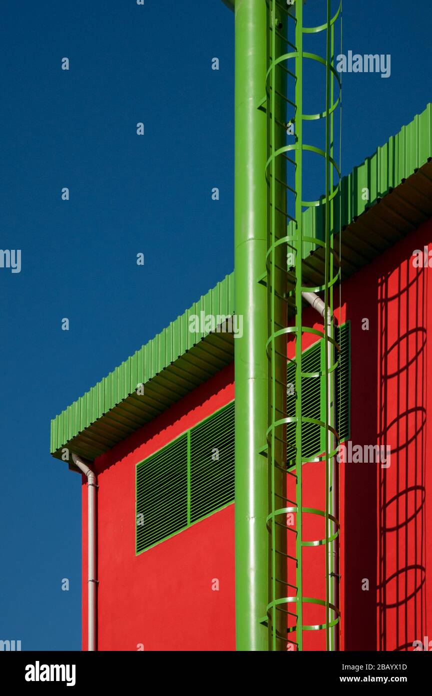 Industrieschornsteine, die zu einem Kraftwerk gehören. Das Kraftwerk hat ein leuchtendes rotes Gebäude und grüne Kamine. Stockfoto