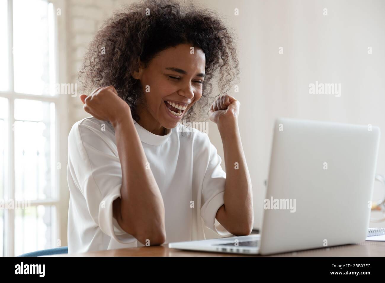 Afrikanische Frau am Schreibtisch sitzt fühlt sich überglücklich an Lesen Sie großartige Nachrichten Stockfoto