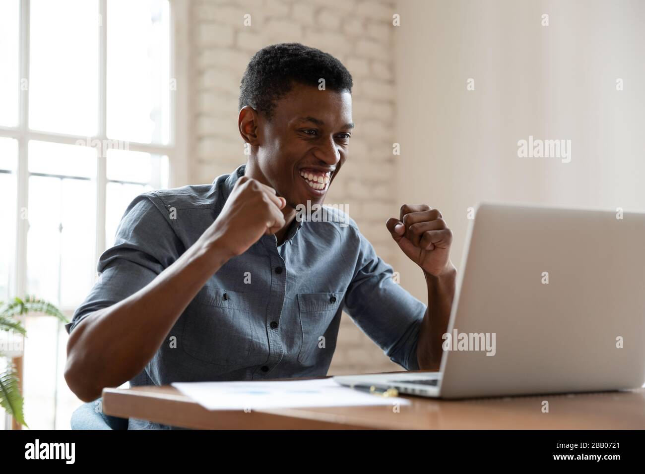 Der afrikanische Geschäftsmann, der am Schreibtisch sitzt, fühlt sich begeistert Lesen Sie großartige Nachrichten Stockfoto