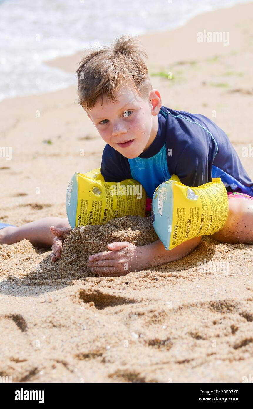 6 Jahre alter kaukasischer Junge mit aufrüttendem Armband, der Spaß hat, im heißen sandigen Strand im Urlaub Varna Bulgarien zu spielen Stockfoto