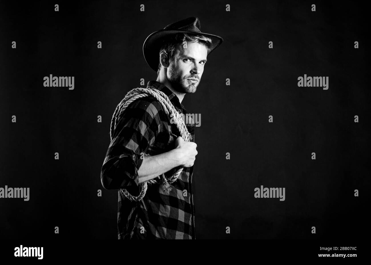 Lasso-Werkzeug des amerikanischen Cowboys. Lasso wird in Rodeos als Teil von Konkurrenzveranstaltungen verwendet. Lasso kann gebunden oder eingewickelt werden. Das westliche Leben. Mann unrasierter Cowboy schwarzer Hintergrund. Mann, der ein Halteseil trägt. Stockfoto