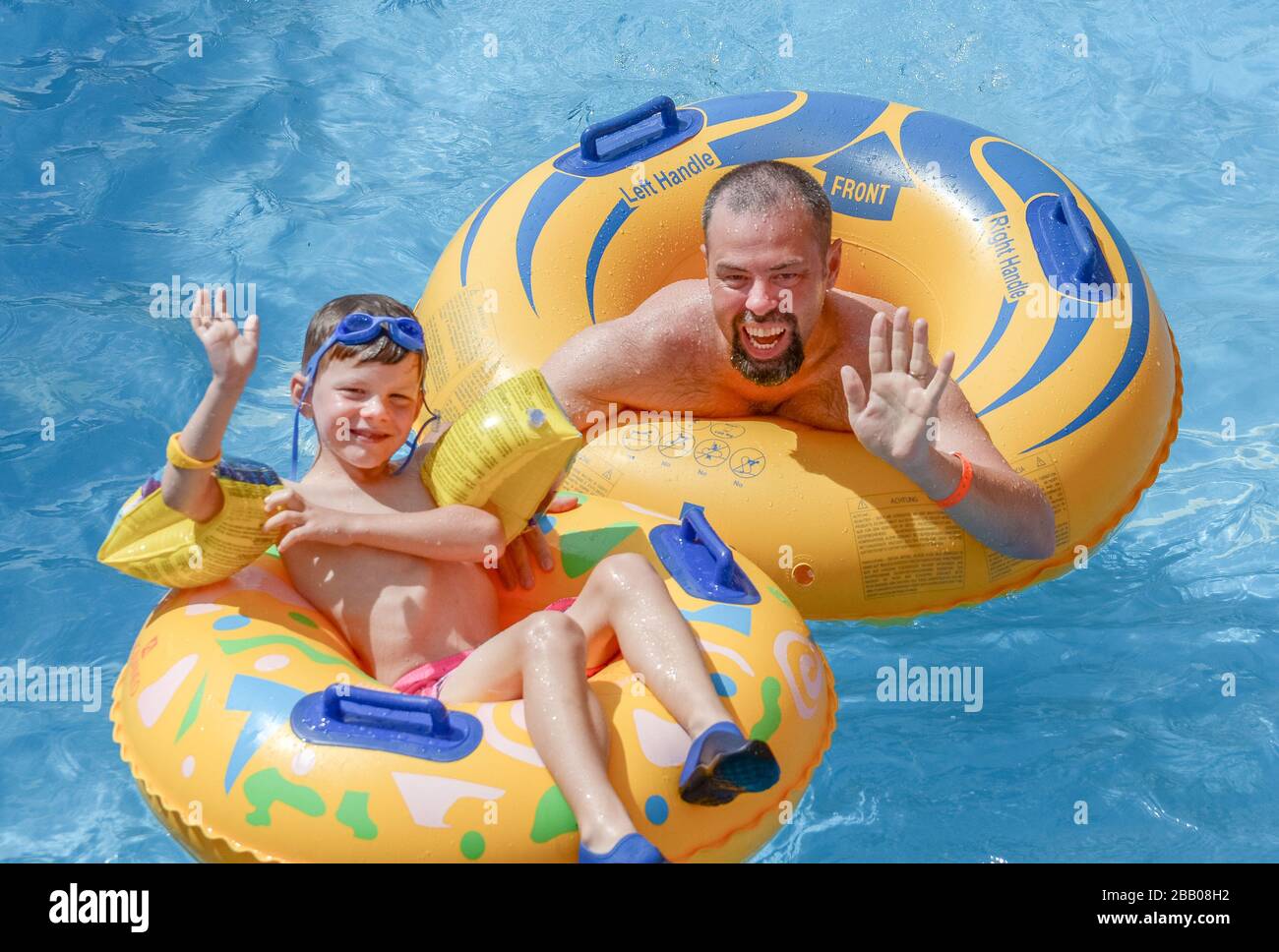 Kaukasischer Vater und Sohn winken vor der Kamera und schweben auf Gummiringen im Wasser-Aqua-Park Warna Bulgarien Stockfoto