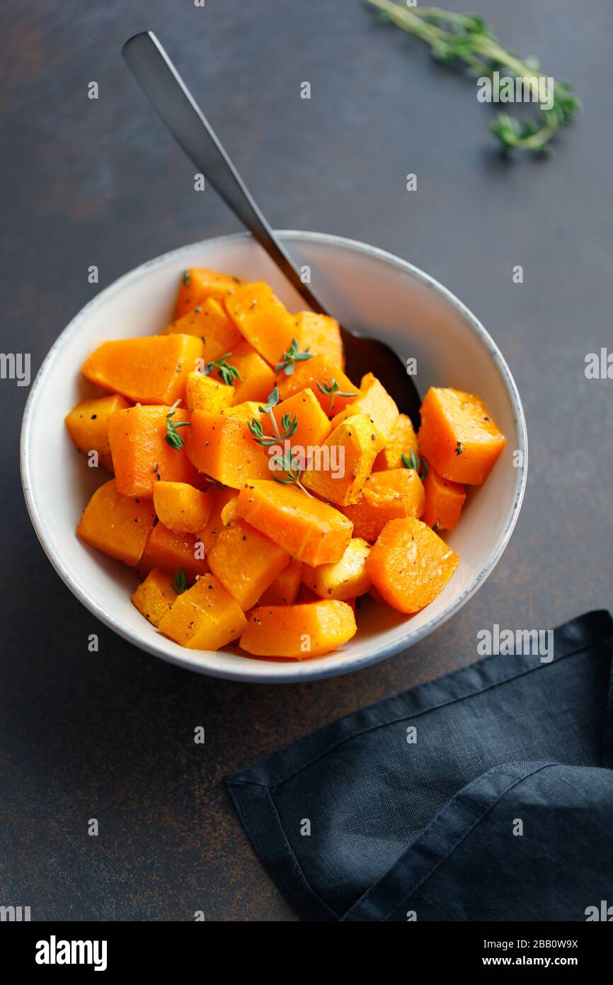 Geröstete Kürbisstücke mit frischem Thymian in einer Keramikschale auf einem Tisch. Saisonales Herbstrezept. Stockfoto