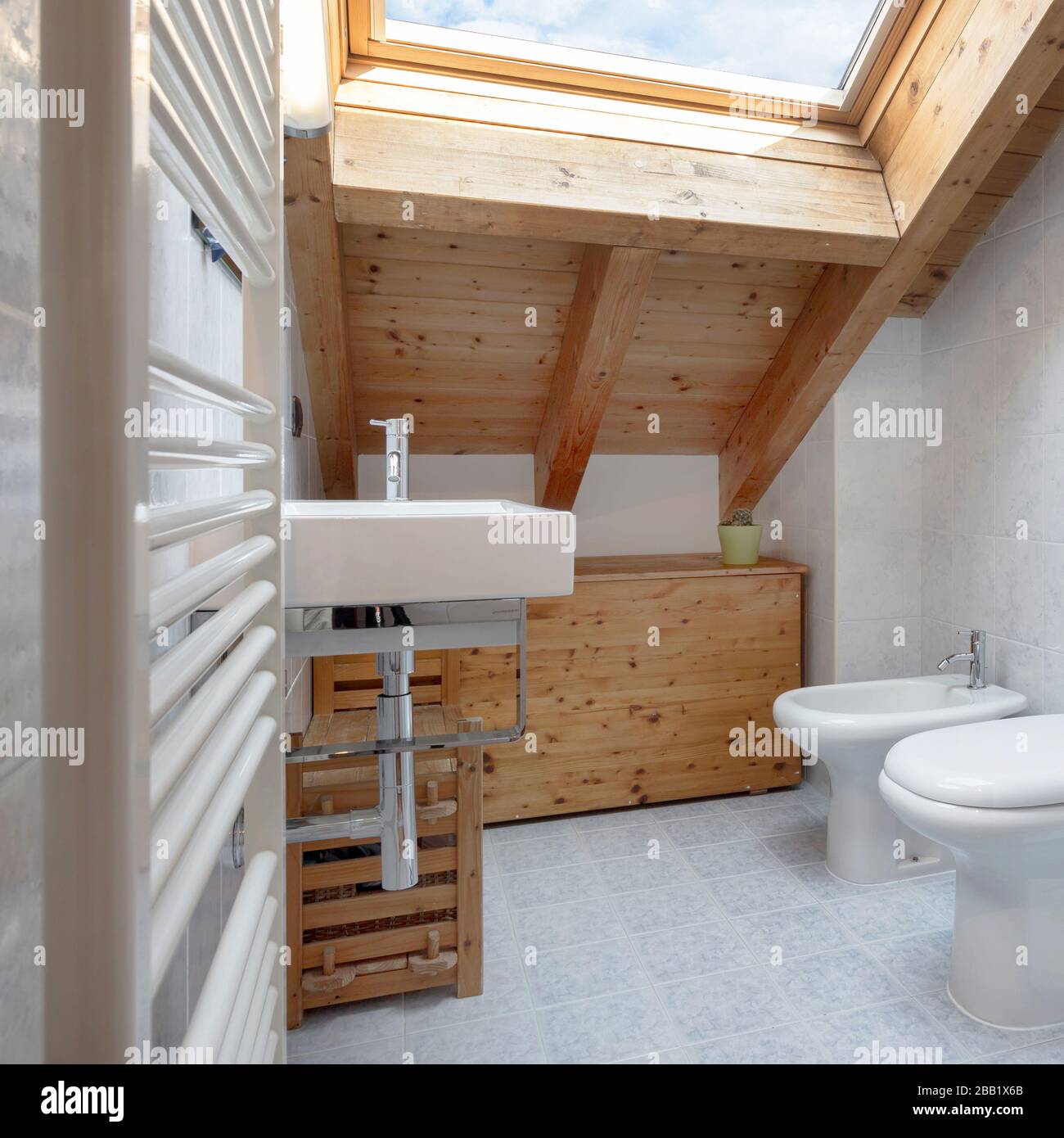 Praktisches und gemütliches Badezimmer mit Handtuchwärmer, toilette, Schrank und Waschbecken. Dach mit freiliegenden Holzbalken und Himmelfenster. Stockfoto
