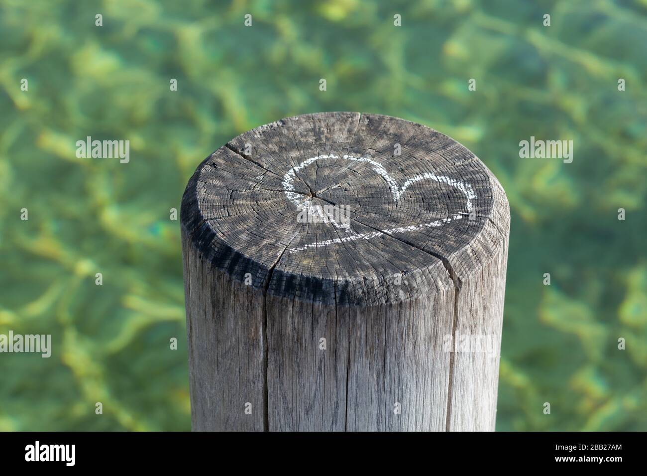 Kreidezeichnung eines Herzsymbols auf einem Holzhaufen eines Stegs. Im Hintergrund grünes Wasser. Konzept für Liebe, Ehe, sein zusammen, Valentinstag. Stockfoto