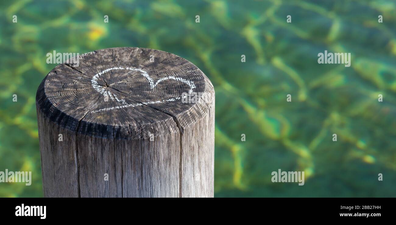 Chalk Zeichnung eines Herzens auf einem rustikalen Holzpfahl/Stapel. Im Hintergrund grün gefärbtes Wasser. Mit Kopierbereich. Kartenmotiv für Liebe, Heirat usw. Stockfoto