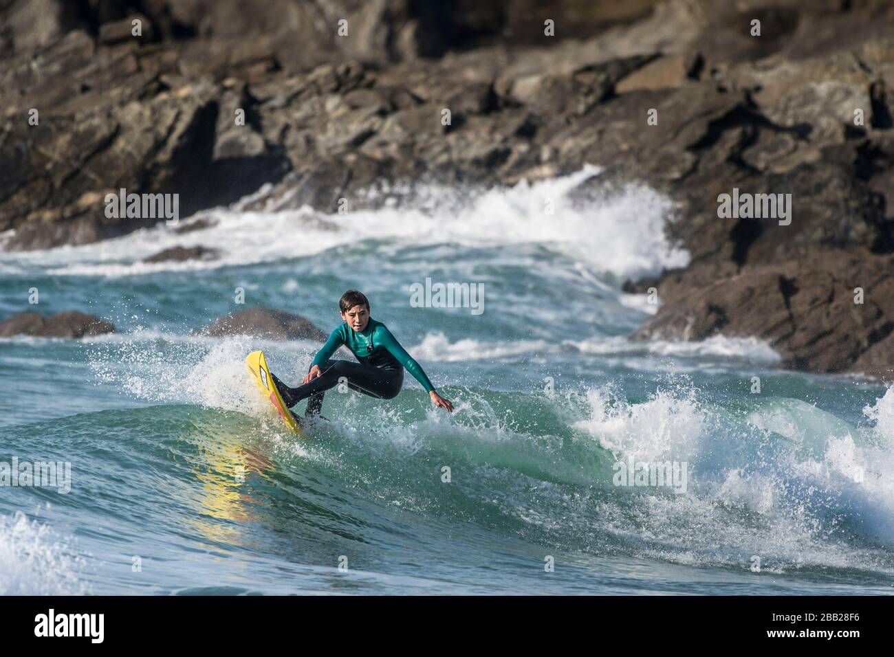 Spektakuläre Surfaktion, während ein junger männlicher Surfer eine Welle in Fistral in Newquay in Cornwall reitet. Stockfoto