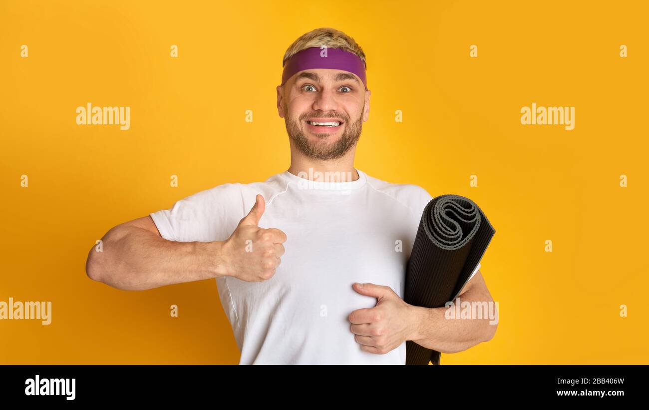 Lächelnder Mann mit Sportmatte mit Daumen nach oben Stockfoto