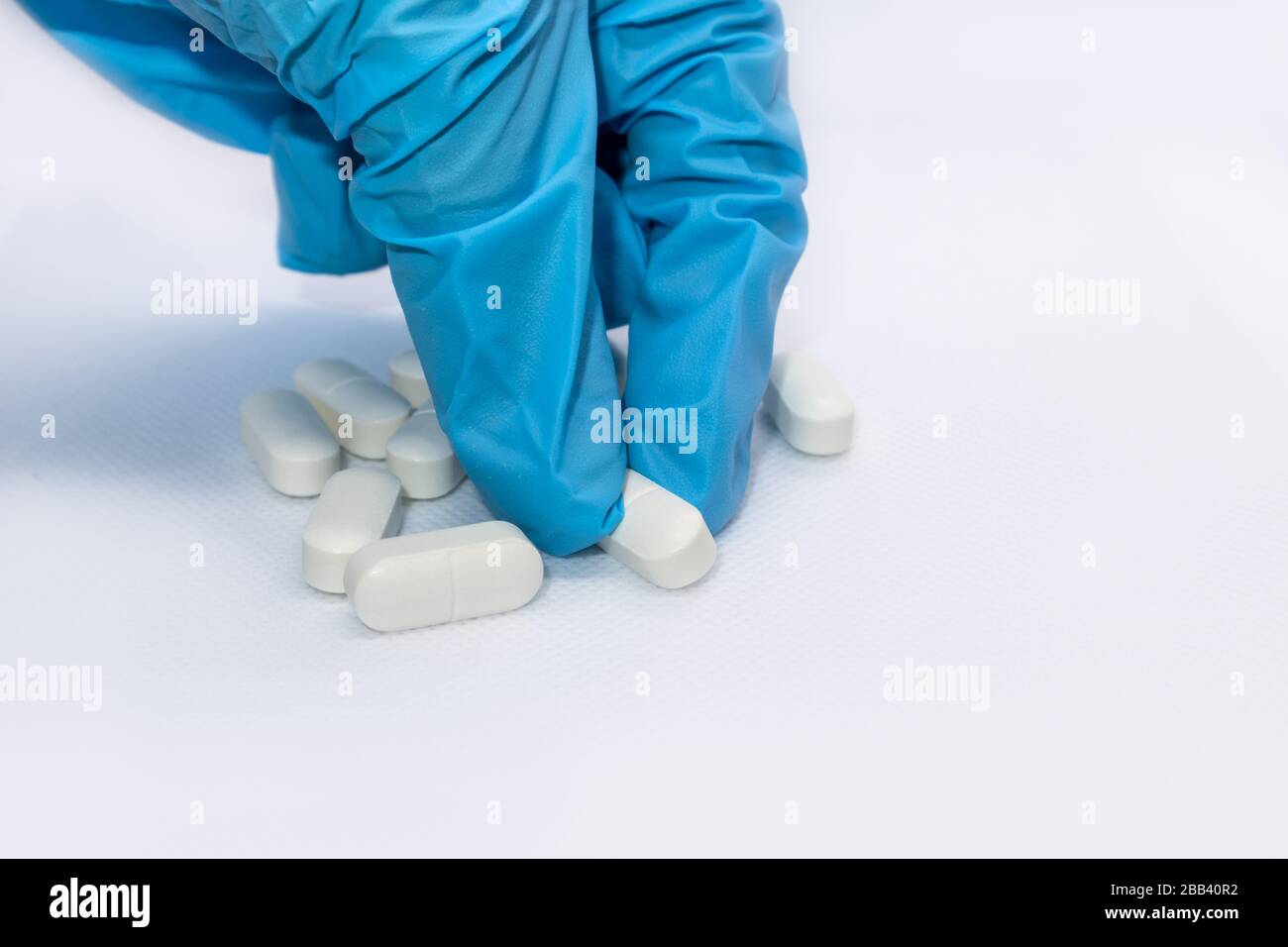 Hand in blau Handschuh nimmt weiße Supplementen lange Pillen auf weißem Hintergrund. Heilmittel Gesundheit Medikament Licht Farben Makro isoliert Nahaufnahme Stockfoto