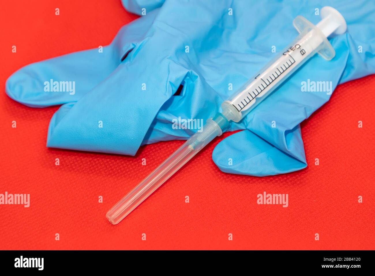 Weißes 2-ml-Spritzenmakro auf roter Oberfläche, blauer Gummihandschuh. Medizinliches Injektions-, Impfstoff- und Heilmittel Stockfoto